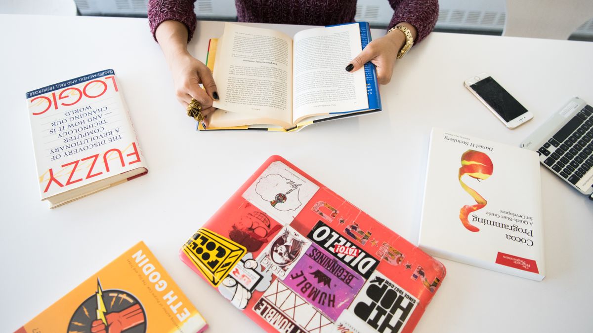 A laptop open next to a dictionary and reference books on a desk
