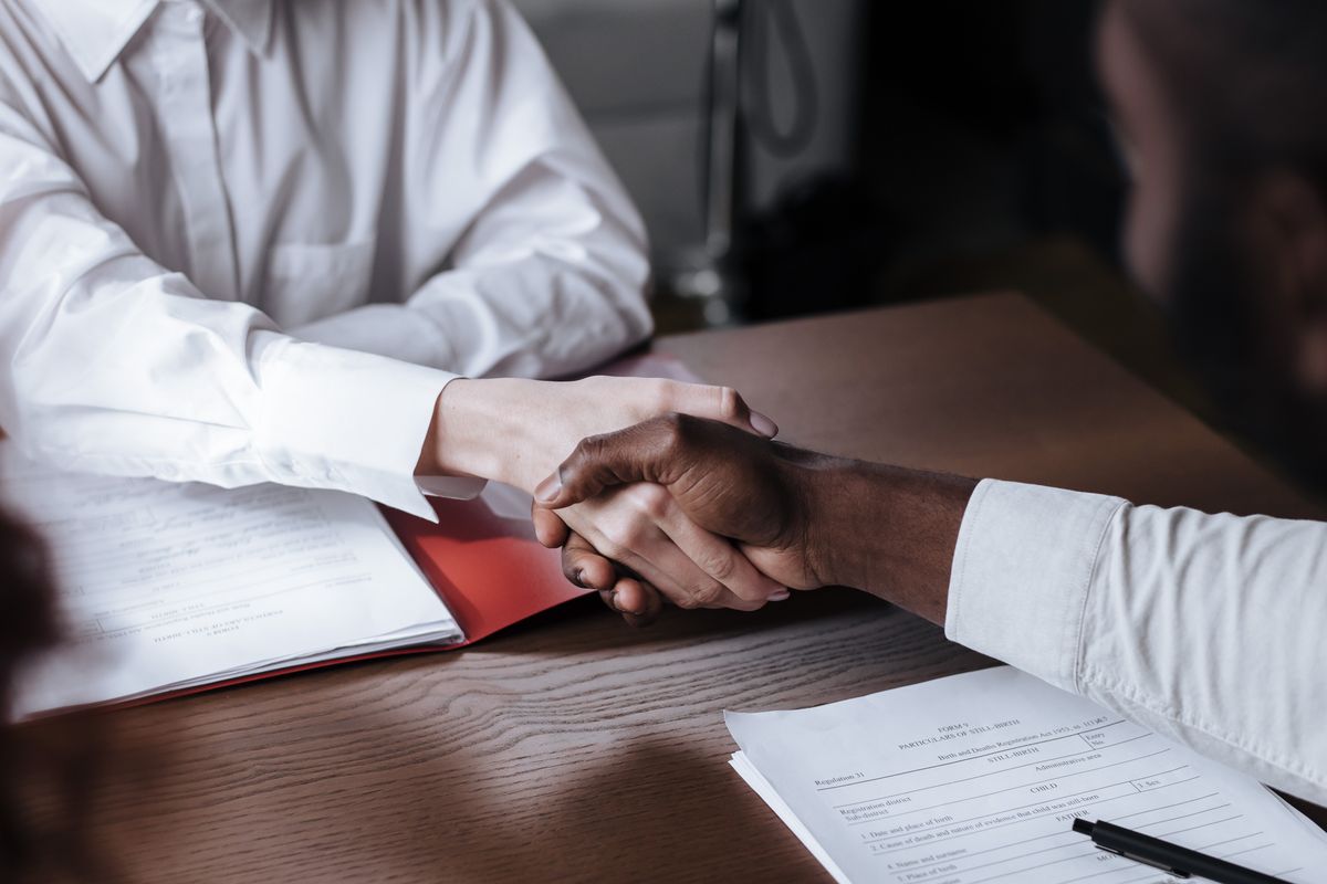 Two business people shaking hands over signed documents